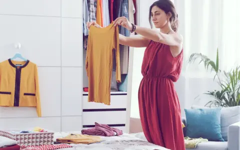 Frau sortiert Kleidung nach der Marie Kondo Methode. Ein gelbes Oberteil wird in die Hand genommen, daneben ein gelber Blazer und ein Korb mit gefalteten Textilien.