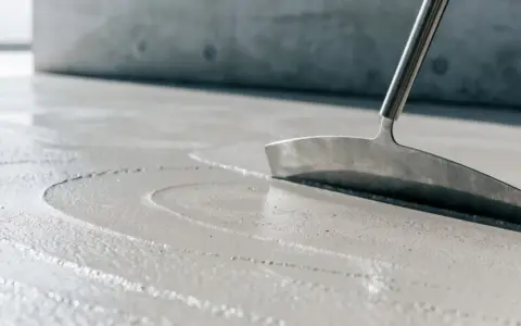 Glatter, nasser Beton wird mit einem Werkzeug bearbeitet, um die Oberfläche für das Beton ausschalen vorzubereiten.