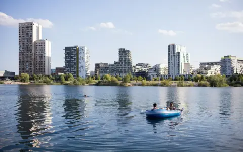 Zwei Männer treiben in einem Schlauchboot auf dem See der Seestadt Aspern. Im Hintergrund ragt die moderne Architektur der Stadt auf.