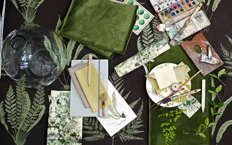 Ein Moodboard mit grünen Stoffen, Aquarellfarben, Pinseln und Farnmotiven. Hier wird gezeigt, was ein Moodboard ist: eine Sammlung von Inspirationen.