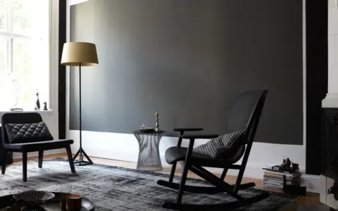 Stilvolles Wohnzimmer mit dunkler wand schwarz streichen Idee. Schwarzer Schaukelstuhl, Sessel, Stehlampe und Teppich.