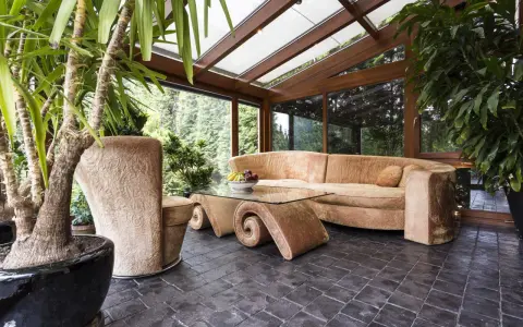 Gemütlicher Wintergarten mit bequemer Couch und Glascouchtisch. Pflanzen und viel Licht schaffen eine entspannte Atmosphäre, ideal zum Wintergarten einrichten.