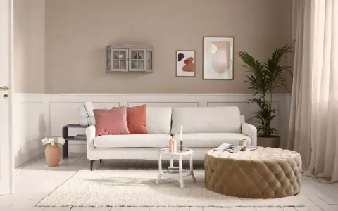 Gemütliches Wohnzimmer mit cremefarbener Couch, passenden Kissen und einem Hocker. Die ecru farbe kombinieren sich harmonisch mit den Wandfarben und Deko-Elementen.