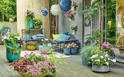 Bunte Blumen und grüne Pflanzen auf einer Terrasse, mit Hängekörben und Kissen. Tolle gartendeko ideen für Ihr Zuhause.