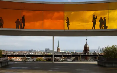 Silhouetten von Menschen auf dem Regenbogenpanorama des Kunstmuseums Aarhus. Blick auf die Stadt und das Meer.