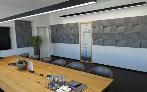 Moderne Konferenzraumgestaltung mit Akustikpaneelen an der Wand, um den **Schall im Raum zu reduzieren**. Ein großer Holztisch mit Gläsern und Notizbüchern steht im Vordergrund.
