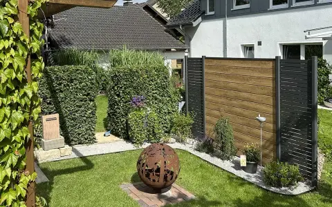 Schöner Garten mit Hecken und Holzzaun als Sichtschutz. Eine Feuerkugel und Pflanzen schaffen Gemütlichkeit. Tolle Ideen für Sichtschutz im Garten.