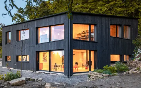 Modernes Haus mit Fassade im Shou Sugi Ban Stil. Große Fenster lassen warmes Licht herein.