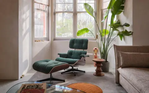 Gemütliches mid century wohnzimmer mit einem dunkelgrünen Sessel und Hocker, einer großen Zimmerpflanze und einem beigefarbenen Sofa.
