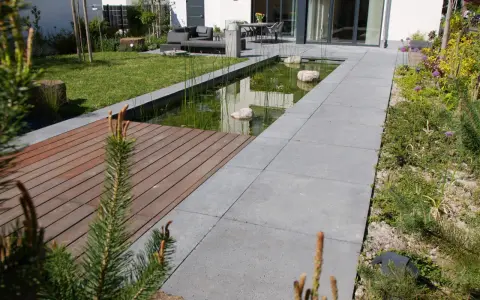 Moderner Vorgarten gestalten: Teich, Holzdeck und Sitzbereich laden zum Entspannen ein. Grüne Rasenflächen und blühende Pflanzen schaffen eine harmonische Atmosphäre.