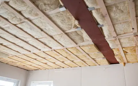 Decke mit Holzbalken und Dämmung. Hier sieht man, was ist Glaswolle: ein isolierendes Material, das in Hohlräume eingebracht wird.