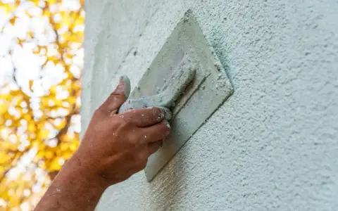 Hand bearbeitet eine Fassade mit einer Kelle. Verschiedene Putztechniken fassade werden hier angewendet, um eine rustikale Textur zu erzeugen.