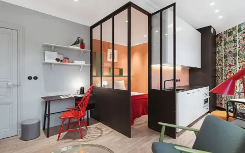 Clever 35 qm wohnung einrichten: Schlafbereich, Küche und Arbeitsplatz sind durch Glaswände getrennt. Bunte Akzente wie der rote Stuhl und die Tapete beleben den Raum.