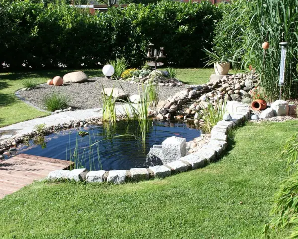 Ein idyllischer kleiner gartenteich ideen mit Steinumrandung, Holzsteg und üppiger Bepflanzung.