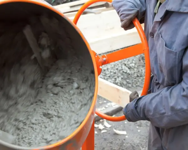 Eine Betonmischmaschine rührt den feuchten Mörtel, der zeigt, aus was Beton besteht: Zement, Wasser und Zuschlagstoffe.