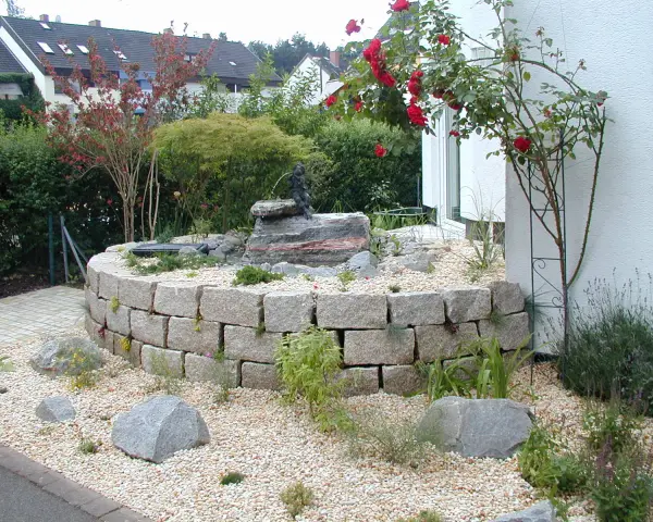 Moderner Hauseingang mit einem geschwungenen Steingarten und einem kleinen Wasserspiel. Ein Hingucker, der zeigt, wie man den Vorgarten modern gestalten kann.