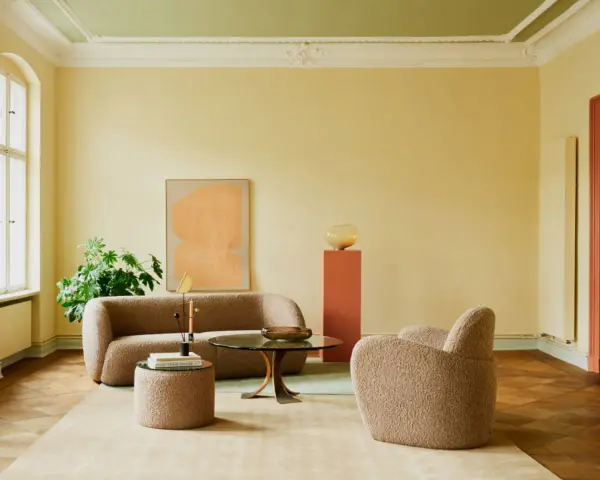Ein Wohnzimmer mit gelben Wänden und einer grünen Decke, die frisch gestrichen wurde. Gemütliche Bouclé-Möbel und ein runder Couchtisch laden zum Verweilen ein.