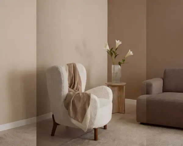 Gemütliches Wohnzimmer mit einem weißen Teddy-Sessel, einer braunen Couch und einer Vase mit Lilien. Warme Farben dominieren die Szene.