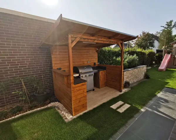 Ein moderner Grillplatz im Garten mit überdachter Holzkonstruktion, Gasgrill und gemütlicher Beleuchtung. Perfekt für Sommerabende.