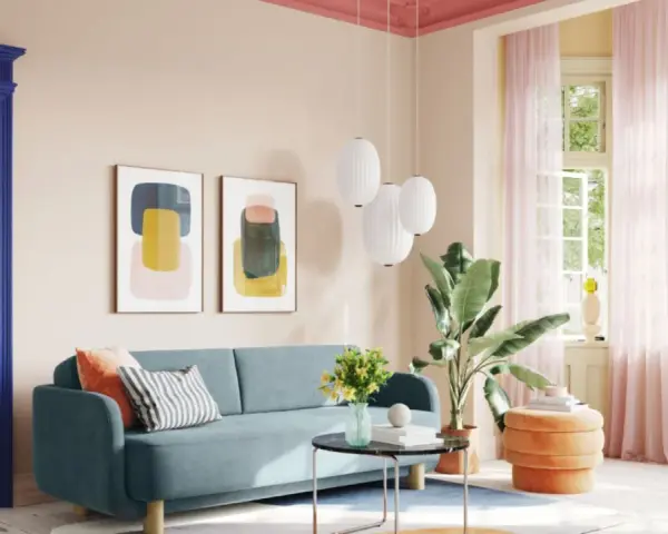 Ein Wohnzimmer mit hellrosa Decke und Wand, blauem Sofa, bunten Bildern und einem Durchgang zu einem Schlafzimmer.