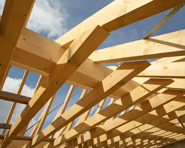 Holzkonstruktion eines Dachstuhls im Bau, mit sichtbaren Balken und Streben. Das Sprengwerk des Dachstuhls wird durch das Sonnenlicht beleuchtet.