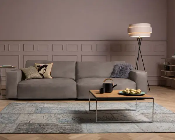 Ein taupefarbenes Sofa mit Kissen und ein Couchtisch mit Obst. Die Wandfarbe ist ein warmes Braun, das zeigt, welche Farbe passt zu Taupe.