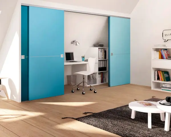 Ein kleines Arbeitszimmer einrichten: Blaue Schiebetüren verbergen einen Schreibtisch mit Laptop und Bürostuhl. Bücherregale und ein Couchtisch ergänzen den Raum.
