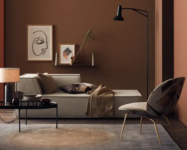 Gemütliches Wohnzimmer mit Sofa, Sessel und Tisch. Die Wände sind in warmen Brauntönen gehalten, die sich mit den Textilien und Dekorationen **braun mischen**.
