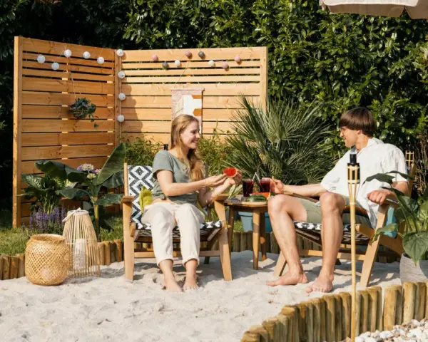 Ein Paar genießt den Sommer mit Wassermelone und Drinks im Garten. Sand, Holz und Pflanzen schaffen ein echtes Strandfeeling im Garten.