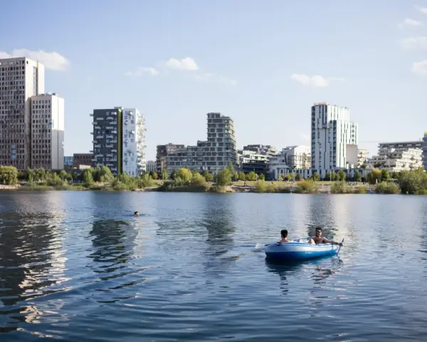 Zwei Männer treiben in einem Schlauchboot auf dem See der Seestadt Aspern. Im Hintergrund ragt die moderne Architektur der Stadt auf.