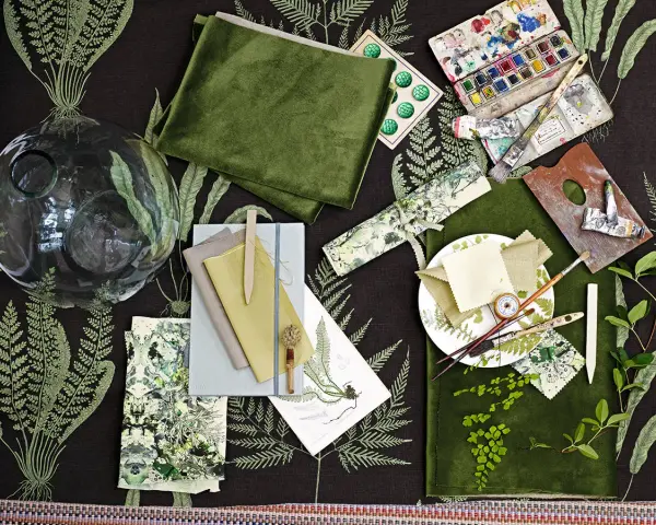 Ein Moodboard mit grünen Stoffen, Aquarellfarben, Pinseln und Farnmotiven. Hier wird gezeigt, was ein Moodboard ist: eine Sammlung von Inspirationen.