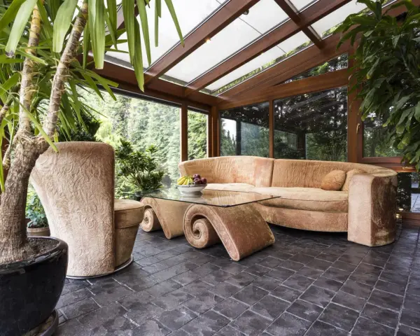 Gemütlicher Wintergarten mit bequemer Couch und Glascouchtisch. Pflanzen und viel Licht schaffen eine entspannte Atmosphäre, ideal zum Wintergarten einrichten.