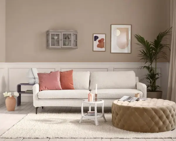 Gemütliches Wohnzimmer mit cremefarbener Couch, passenden Kissen und einem Hocker. Die ecru farbe kombinieren sich harmonisch mit den Wandfarben und Deko-Elementen.