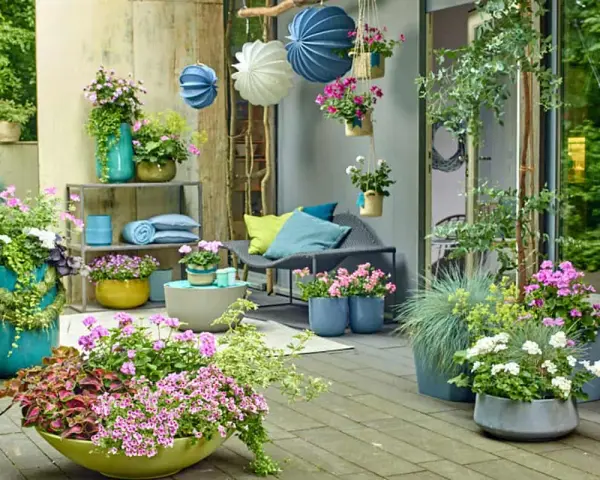 Bunte Blumen und grüne Pflanzen auf einer Terrasse, mit Hängekörben und Kissen. Tolle gartendeko ideen für Ihr Zuhause.