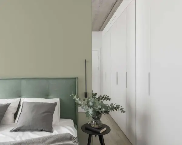 Ein Schlafzimmer mit einer Wand in hellem Olivgrün und einem Bett mit grünem Kopfteil. Der Unterschied zwischen Khaki und Oliv ist hier subtil, aber präsent.