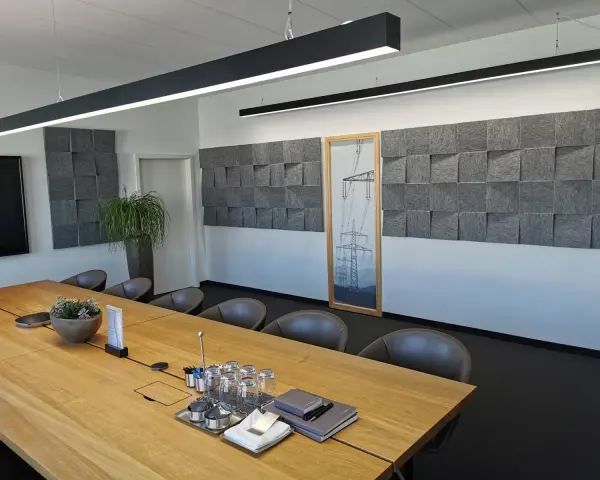 Moderne Konferenzraumgestaltung mit Akustikpaneelen an der Wand, um den **Schall im Raum zu reduzieren**. Ein großer Holztisch mit Gläsern und Notizbüchern steht im Vordergrund.