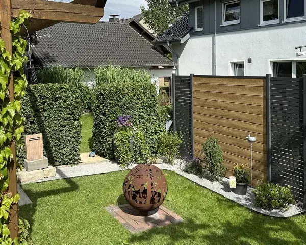Schöner Garten mit Hecken und Holzzaun als Sichtschutz. Eine Feuerkugel und Pflanzen schaffen Gemütlichkeit. Tolle Ideen für Sichtschutz im Garten.