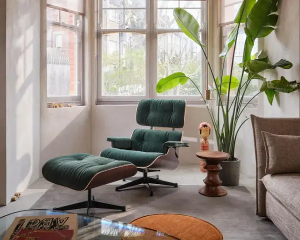 Gemütliches mid century wohnzimmer mit einem dunkelgrünen Sessel und Hocker, einer großen Zimmerpflanze und einem beigefarbenen Sofa.
