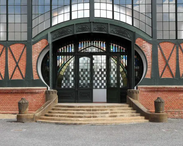 Eingang im artdeco stil mit Ziegelmauerwerk, geschwungenen Metallverzierungen und einem beeindruckenden Buntglasfenster.