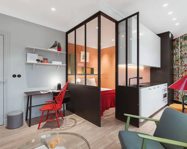 Clever 35 qm wohnung einrichten: Schlafbereich, Küche und Arbeitsplatz sind durch Glaswände getrennt. Bunte Akzente wie der rote Stuhl und die Tapete beleben den Raum.