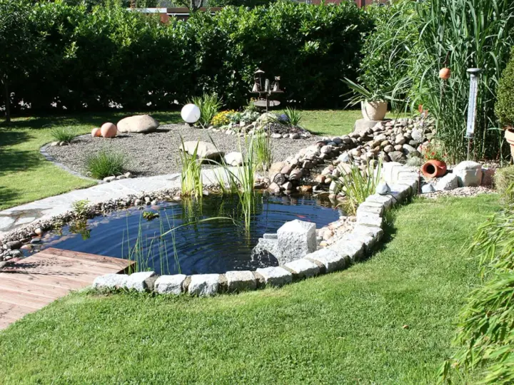 Ein idyllischer kleiner gartenteich ideen mit Steinumrandung, Holzsteg und üppiger Bepflanzung.