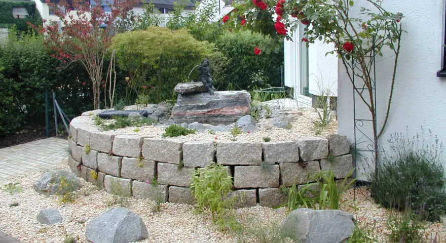 Moderner Hauseingang mit einem geschwungenen Steingarten und einem kleinen Wasserspiel. Ein Hingucker, der zeigt, wie man den Vorgarten modern gestalten kann.
