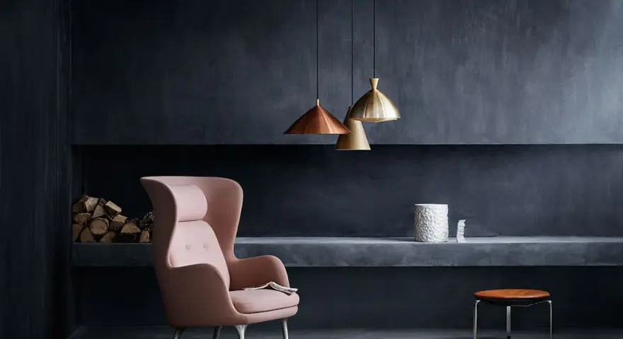 Ein rosafarbener Sessel vor einer anthrazitfarbenen Wand. Die Frage, welche Farbe passt zu Anthrazit, wird hier elegant beantwortet: Zarte Pastelltöne wie dieses Rosa schaffen einen stilvollen Kontrast.