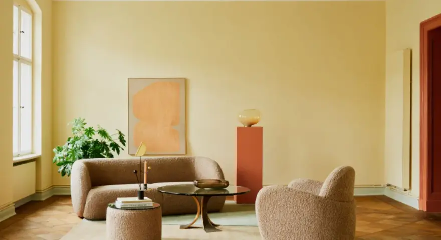Ein Wohnzimmer mit gelben Wänden und einer grünen Decke, die frisch gestrichen wurde. Gemütliche Bouclé-Möbel und ein runder Couchtisch laden zum Verweilen ein.