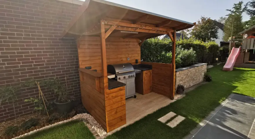Ein moderner Grillplatz im Garten mit überdachter Holzkonstruktion, Gasgrill und gemütlicher Beleuchtung. Perfekt für Sommerabende.