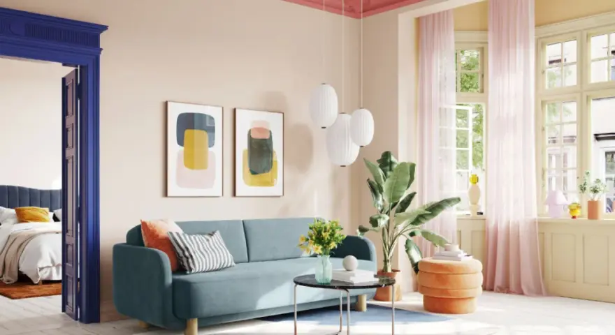 Ein Wohnzimmer mit hellrosa Decke und Wand, blauem Sofa, bunten Bildern und einem Durchgang zu einem Schlafzimmer.
