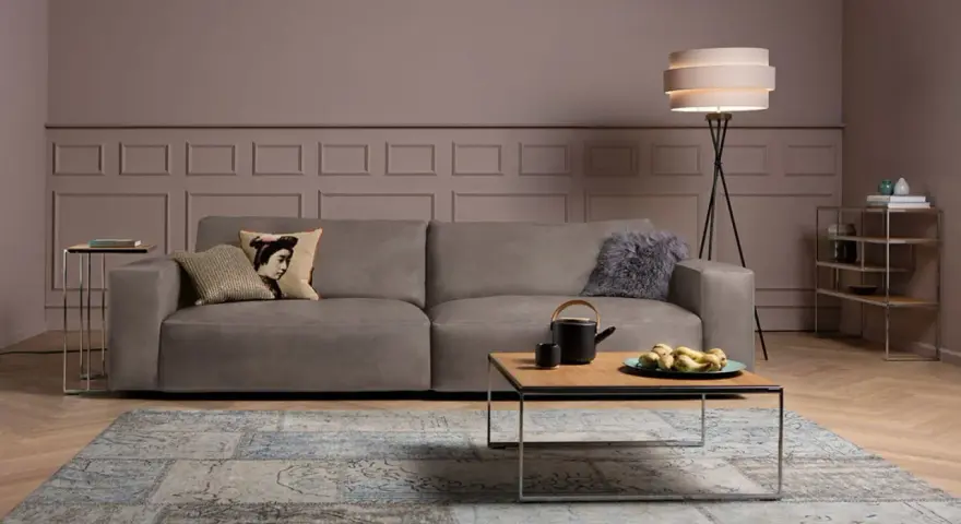 Ein taupefarbenes Sofa mit Kissen und ein Couchtisch mit Obst. Die Wandfarbe ist ein warmes Braun, das zeigt, welche Farbe passt zu Taupe.