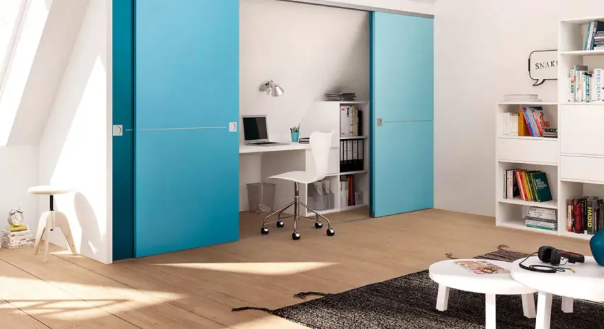 Ein kleines Arbeitszimmer einrichten: Blaue Schiebetüren verbergen einen Schreibtisch mit Laptop und Bürostuhl. Bücherregale und ein Couchtisch ergänzen den Raum.