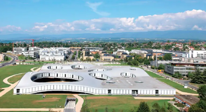 Das Rolex Learning Center in Lausanne, ein futuristisches Gebäude mit runden Öffnungen im Dach, umgeben von grünen Flächen und moderner Architektur.