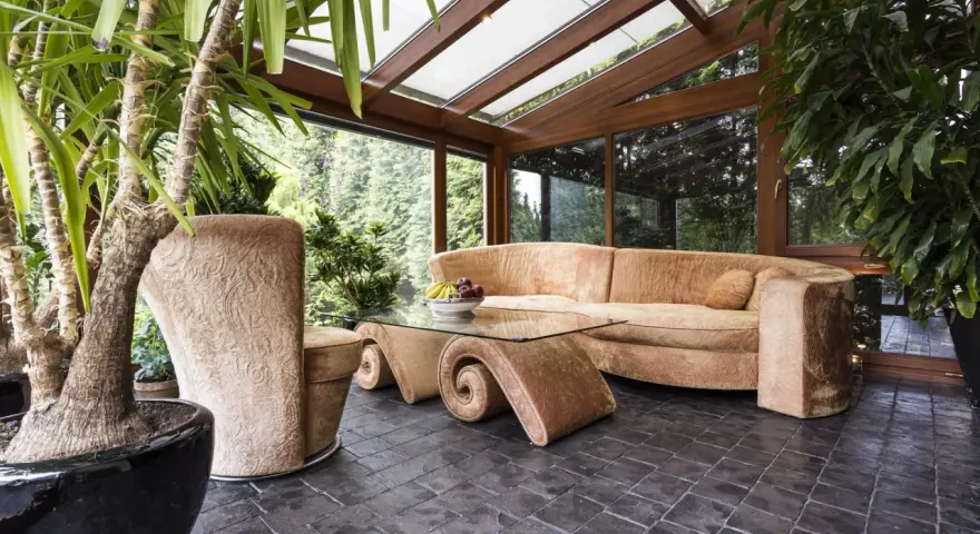 Gemütlicher Wintergarten mit bequemer Couch und Glascouchtisch. Pflanzen und viel Licht schaffen eine entspannte Atmosphäre, ideal zum Wintergarten einrichten.